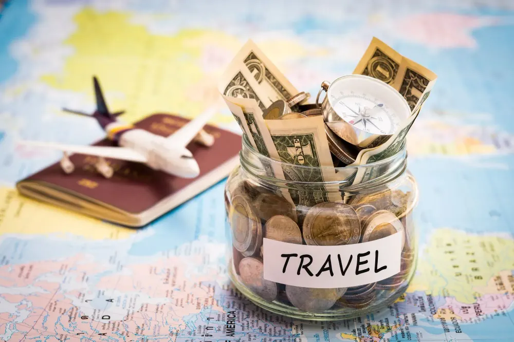 A jar of money labeled "Travel", a passport, and an airplane figurine on a colorful world map